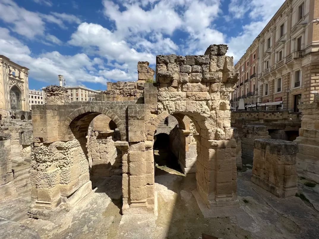 The ancient Roman ruins of the Amphitheatre of Lecce are visible in the heart of the city, surrounded by modern buildings.
