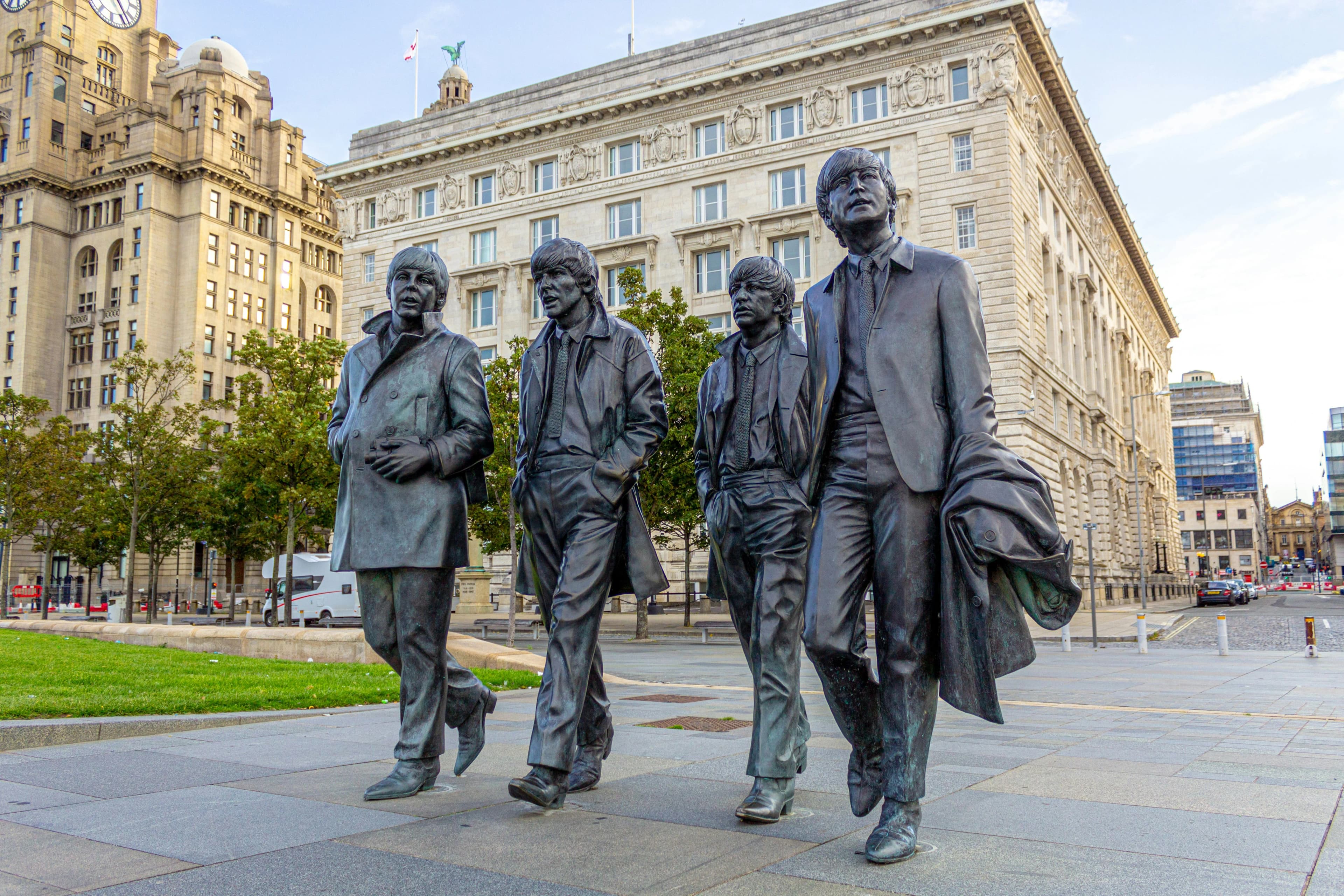 The bronze statues of The Beatles stand in a line at the waterfront, a famous landmark celebrating the city's musical heritage.