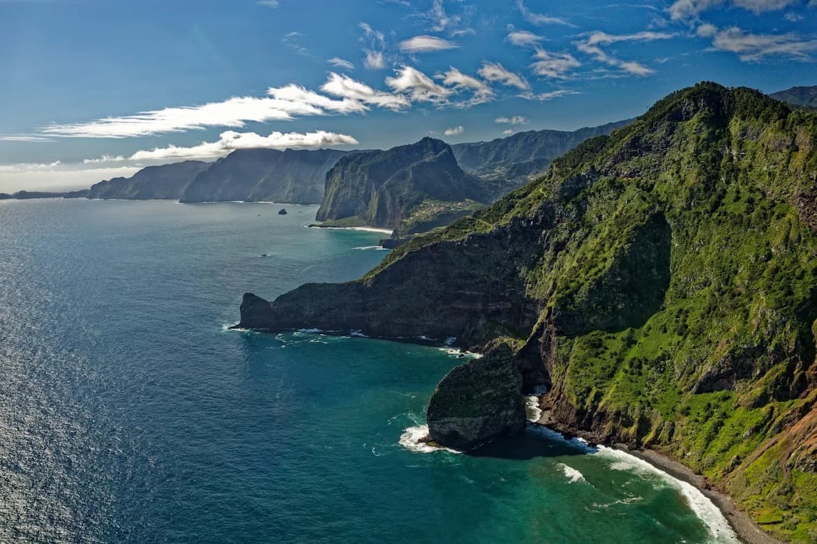 The dramatic, sheer cliffs of the Madeira coastline plunge into the deep blue water, with the Atlantic Ocean stretching to the horizon.