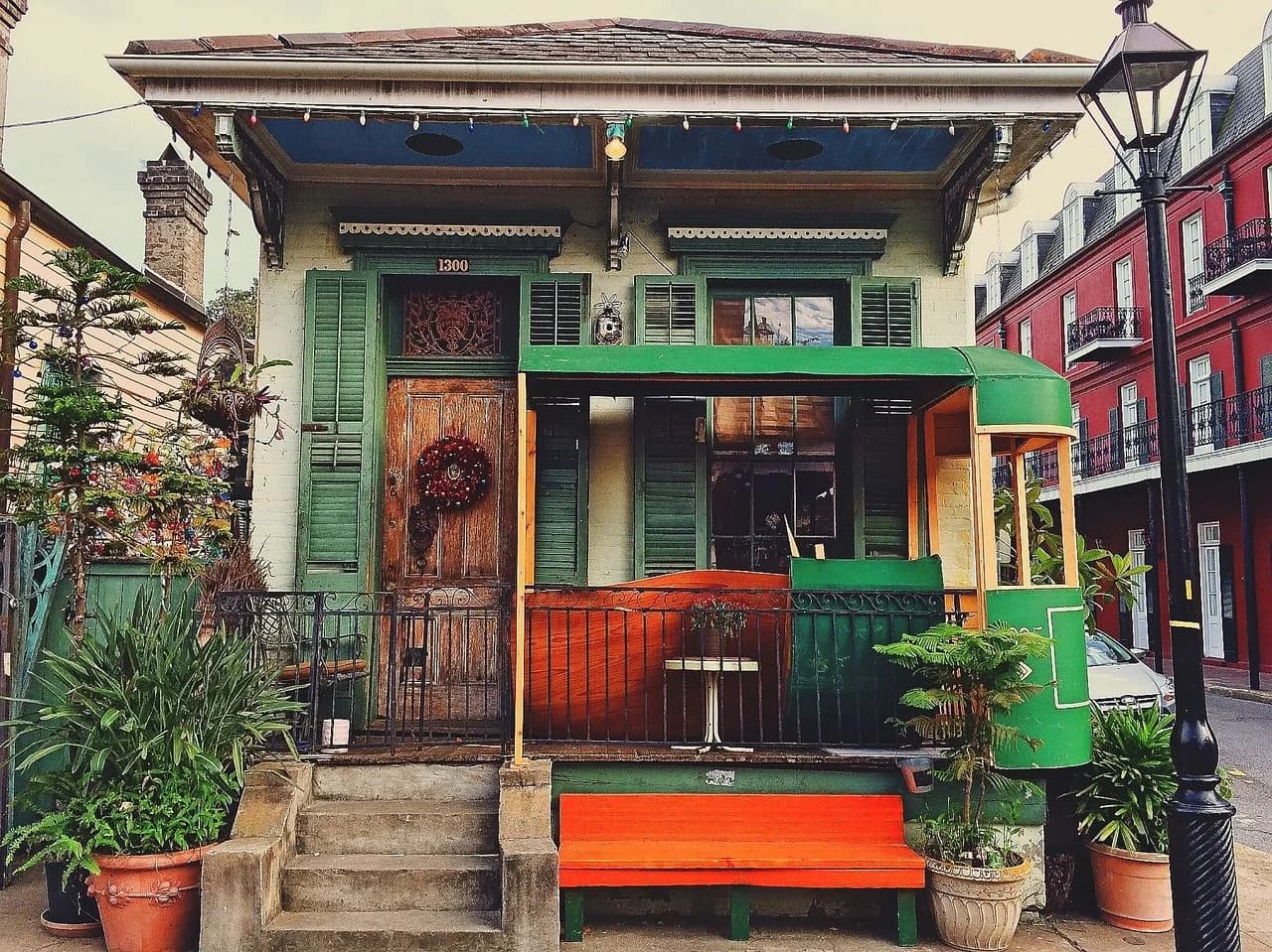 A traditional Creole cottage with a bright orange bench and lush potted plants is a highlight of a historic city street.