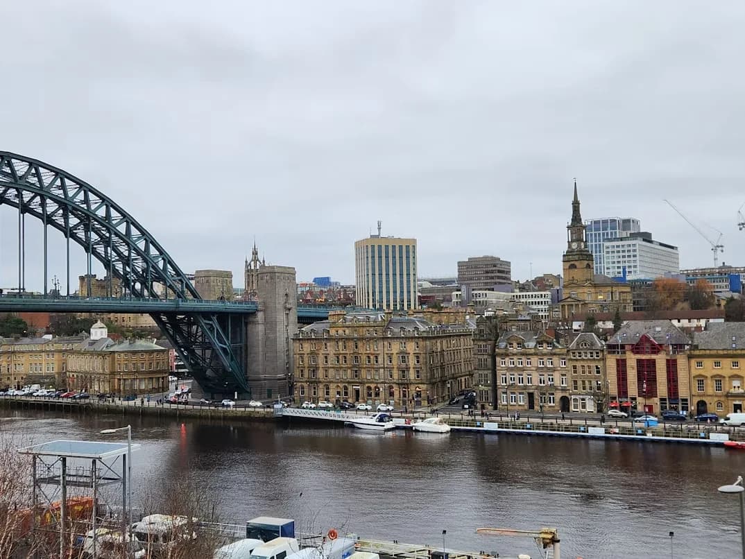 The Tyne Bridge, a massive steel arch bridge, is a prominent feature of the Newcastle skyline, with historic buildings lining the riverbank.