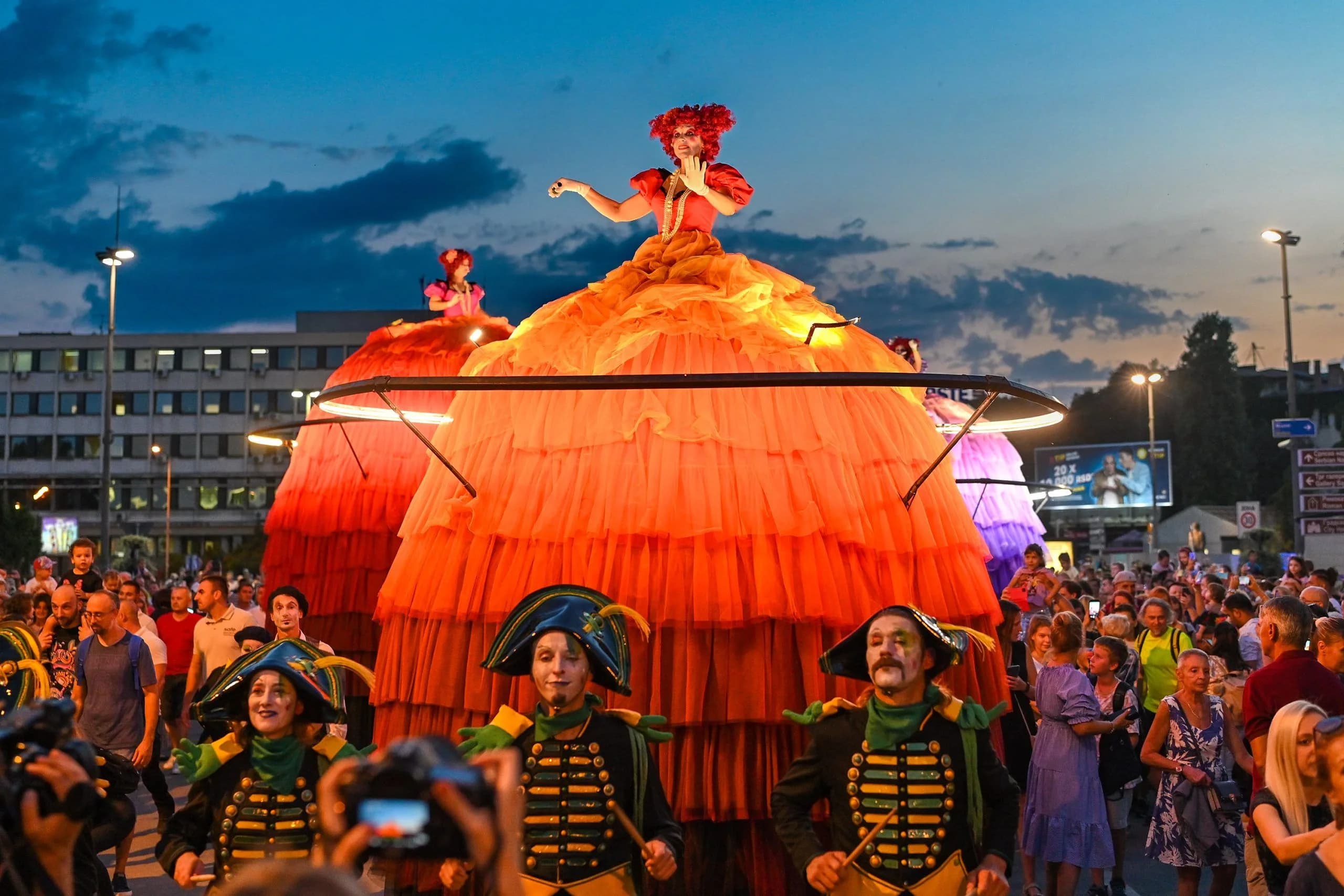People dressed in elaborate, colorful costumes perform on stilts in a city street, a highlight of a local festival.