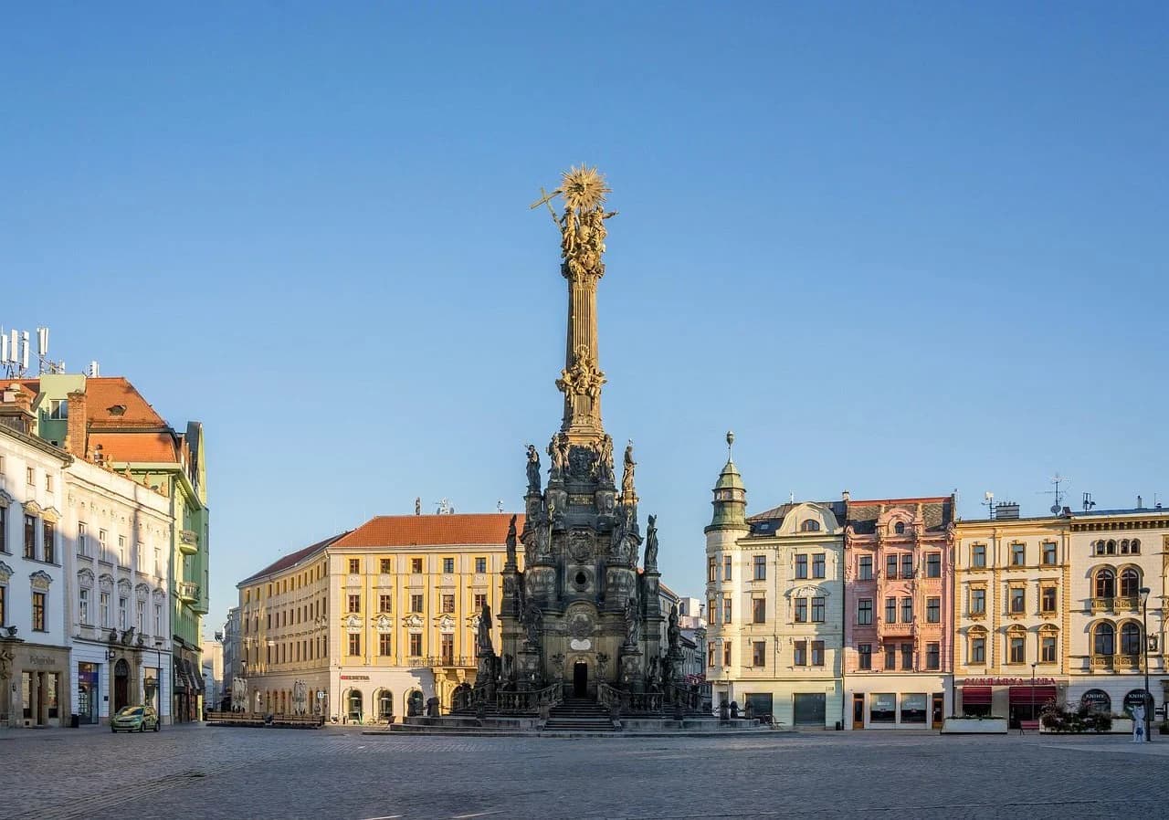 The Holy Trinity Column, a UNESCO World Heritage site, stands in a bustling city square, surrounded by historic buildings and cafes.