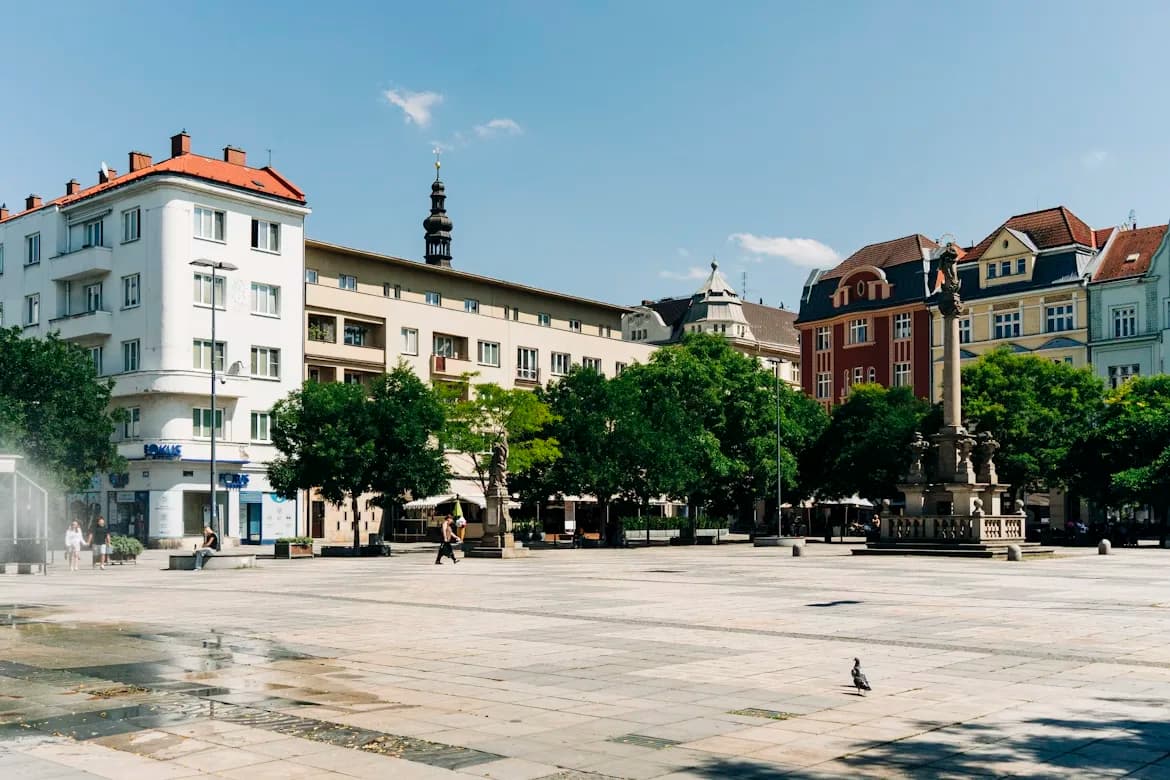 A large, open city square is surrounded by historic buildings and cafes on a sunny day.