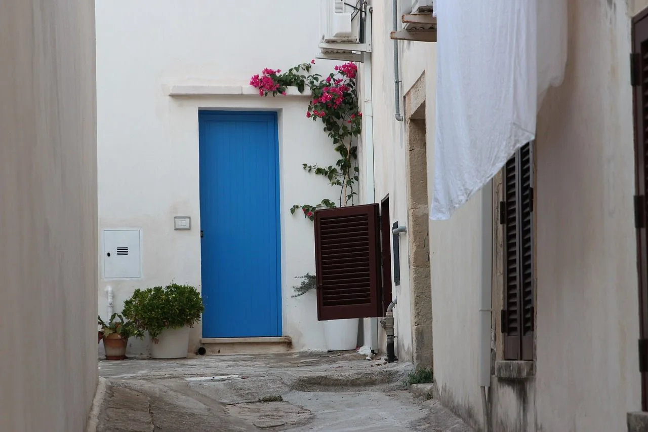 A narrow, white-washed alleyway in Otranto is lined with traditional buildings and a small cafe with outdoor seating.