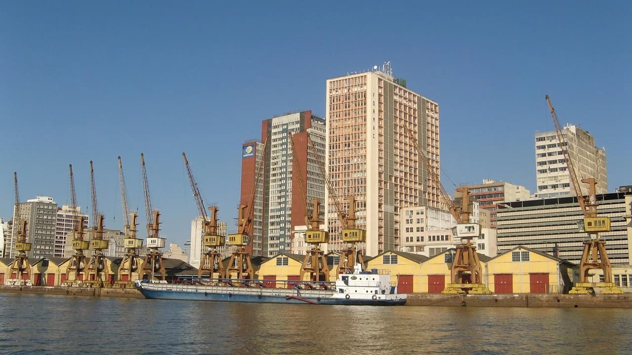 A historic port is bustling with a large number of cranes, with a mix of modern and traditional buildings in the background.