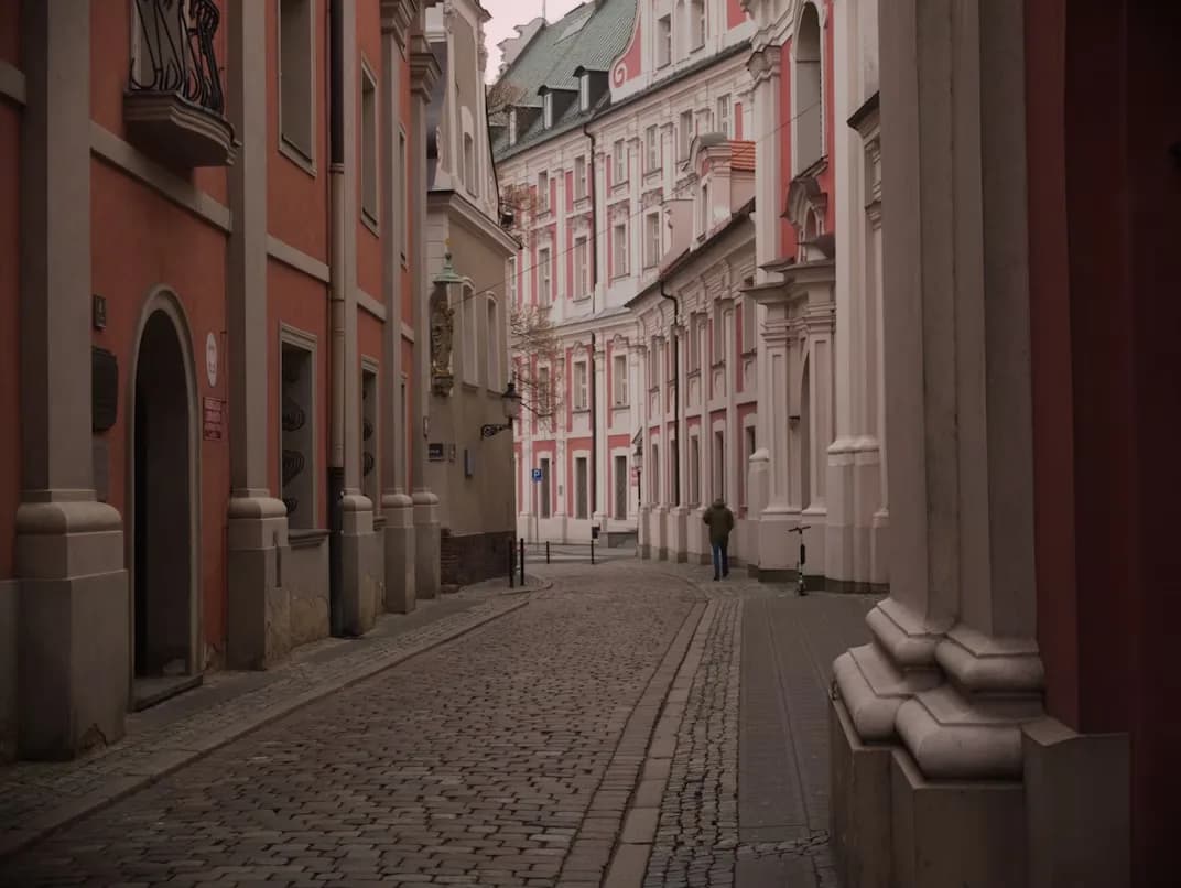 A narrow, cobblestone street in Poznań is lined with elegant red and white buildings.