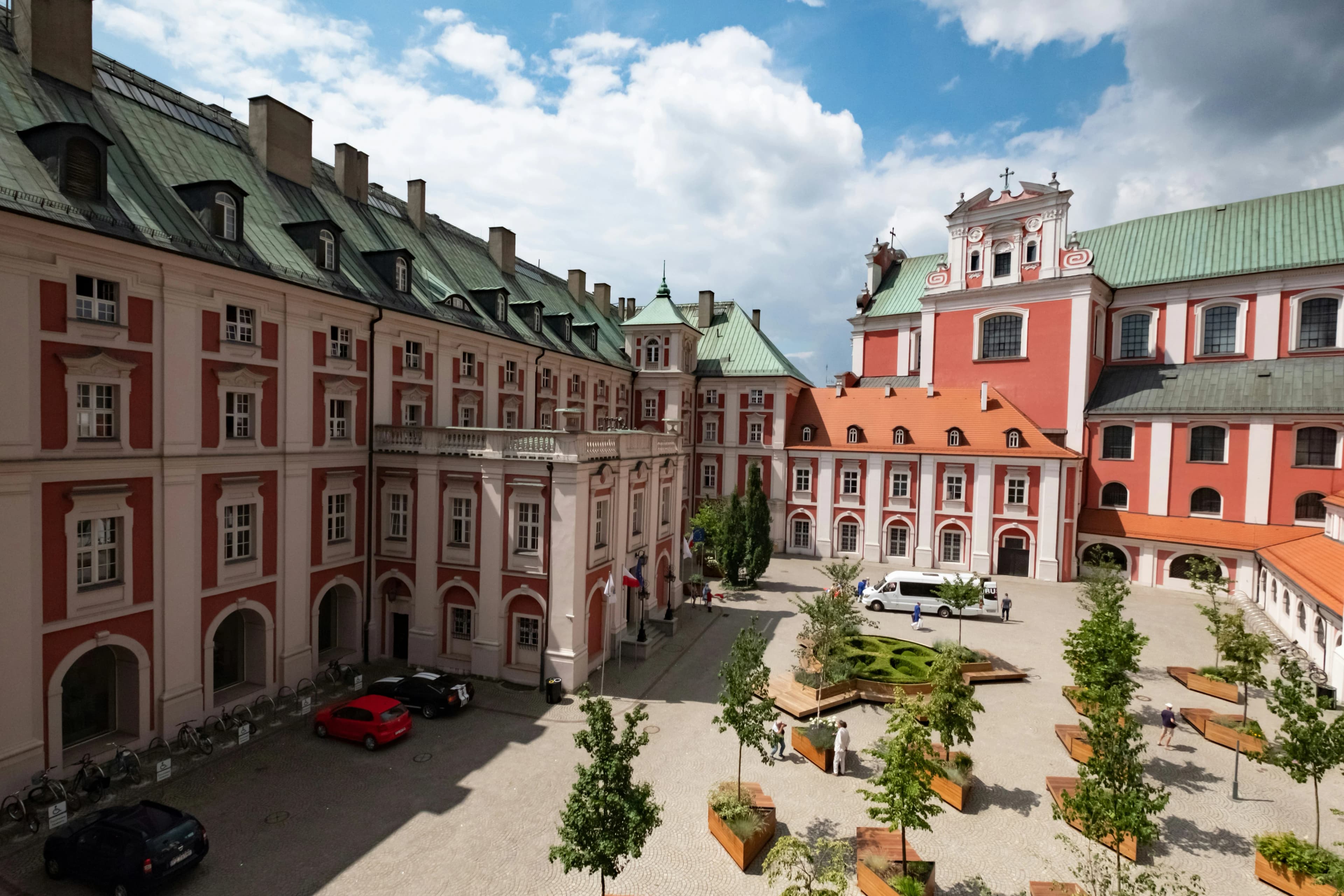The historic city of Poznań is viewed from above, with a large courtyard surrounded by elegant red and white buildings.
