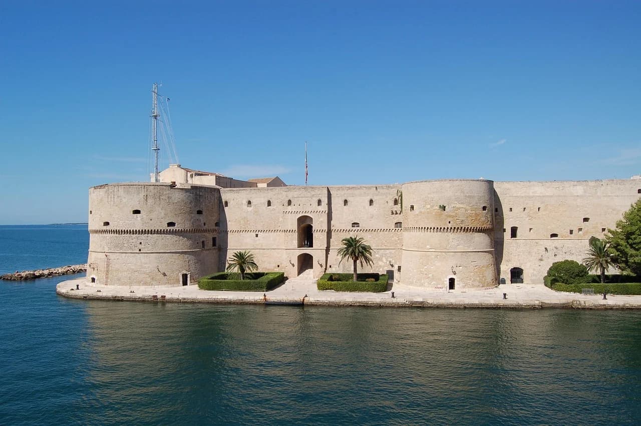 The historic Castello Aragonese, a large stone fortress with four circular towers, stands on a small island in the sea.