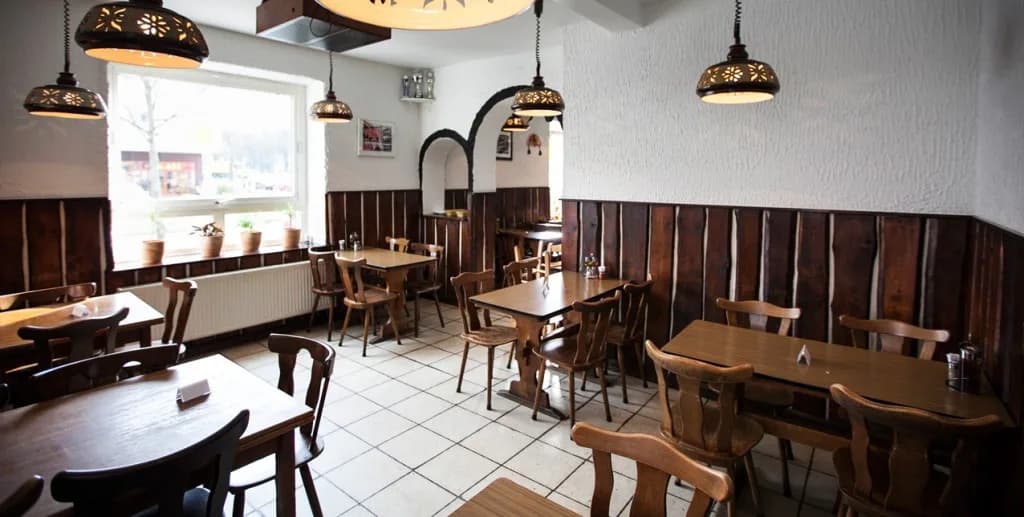 The cozy and simple interior of a traditional restaurant with wooden tables and chairs and a large window.