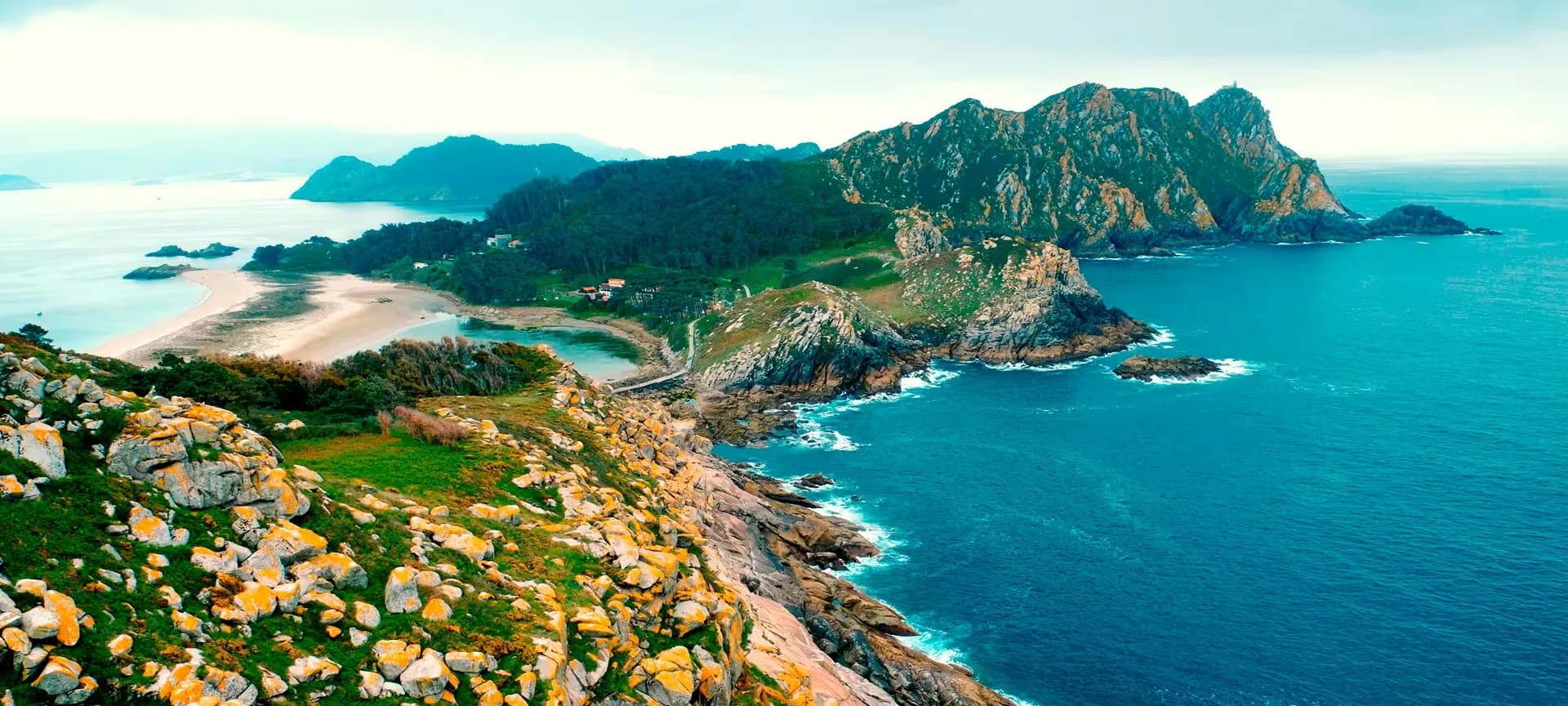 A scenic view of the rugged coastline of the Cies Islands, with white sandy beaches and a beautiful blue ocean.