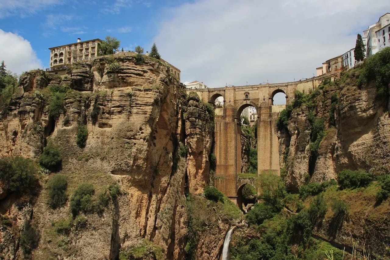 The Puente Nuevo, a magnificent stone bridge with a waterfall below, spans the deep gorge, with the historic buildings of Ronda on either side.