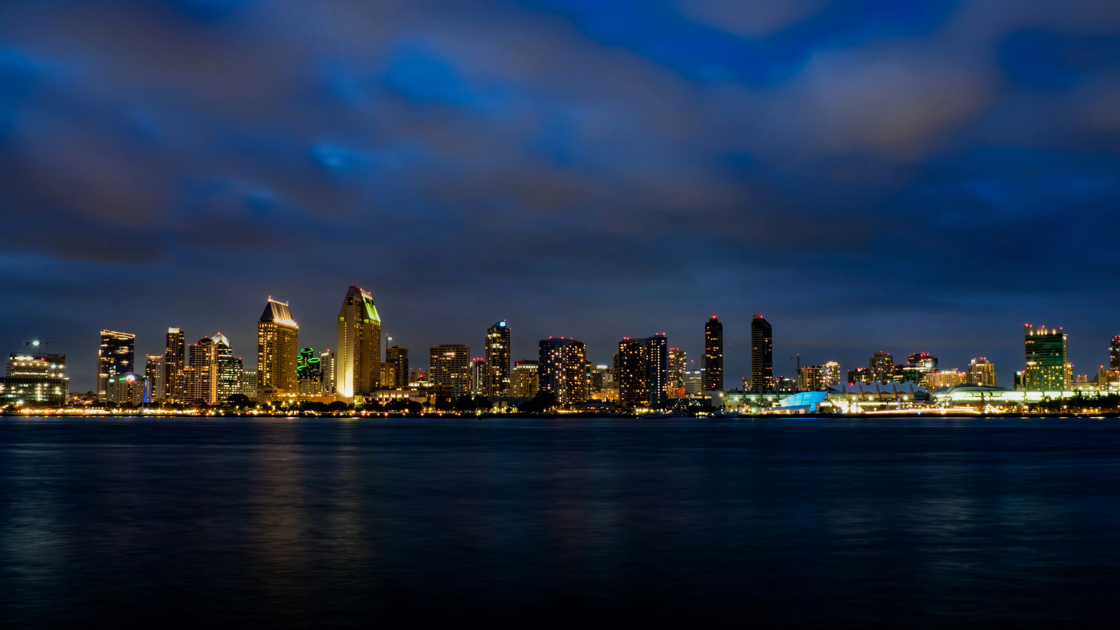 The San Diego skyline is beautifully illuminated at night, with the city lights reflected on the water of the San Diego Bay.