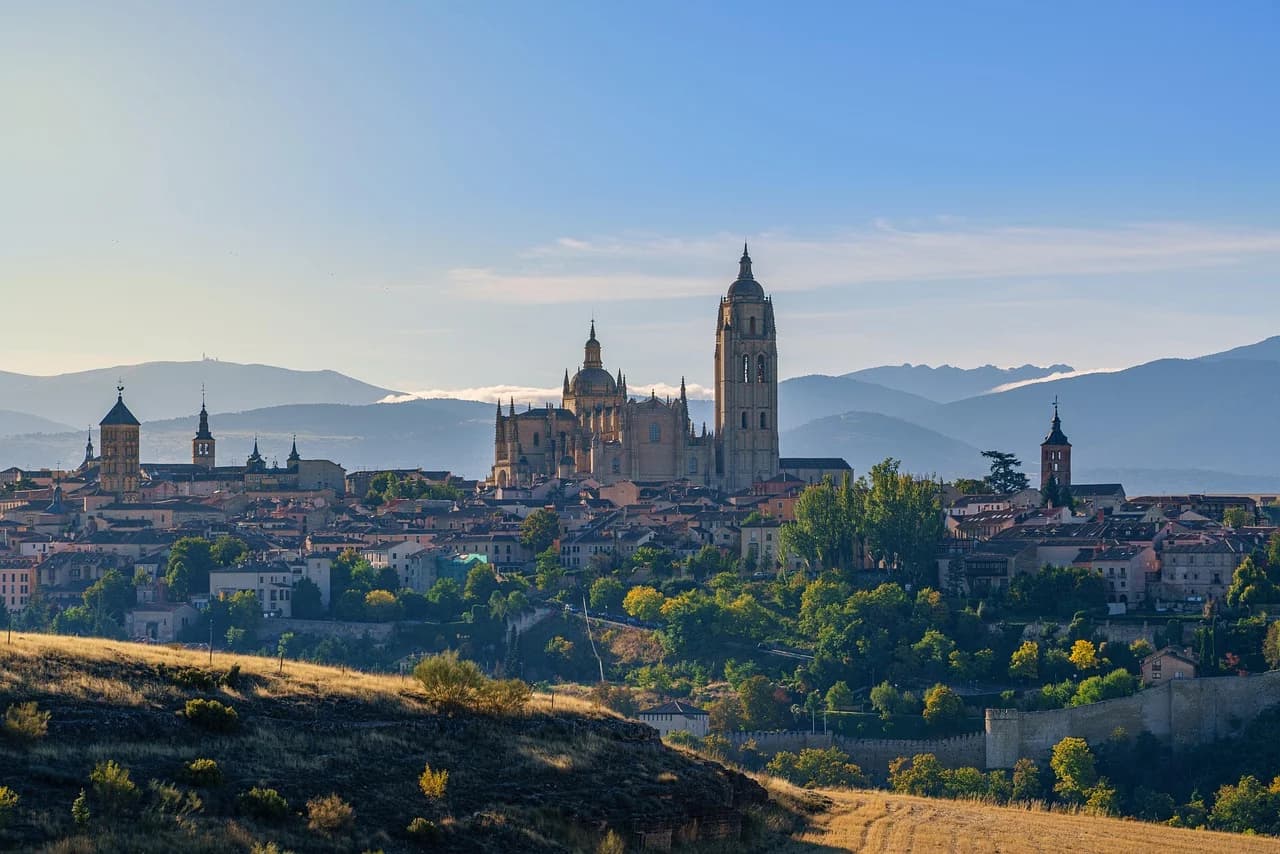 A panoramic view of the Segovia skyline shows the city and its magnificent cathedral from a distance, with a series of hills and mountains in the background.