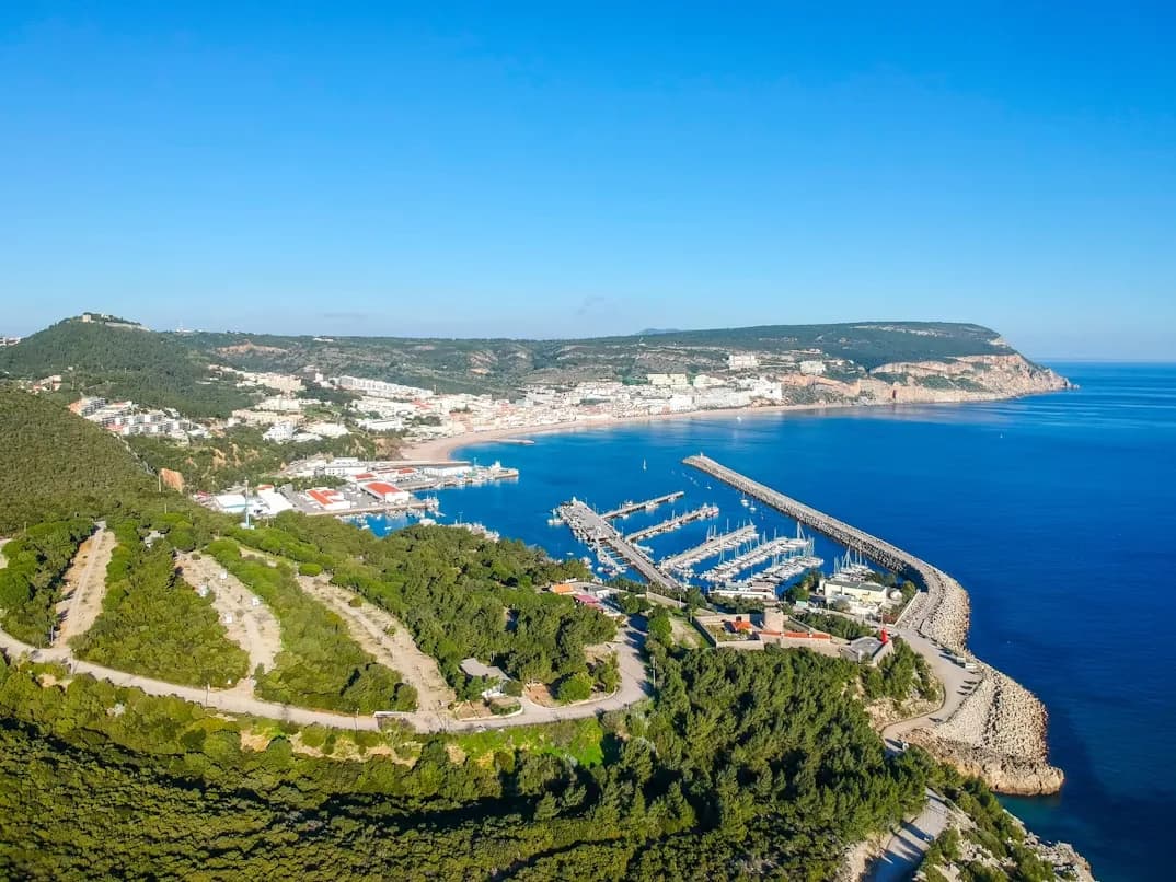 An aerial view captures the bustling port and city of Setúbal, with the Troia Peninsula and the sea stretching to the horizon.