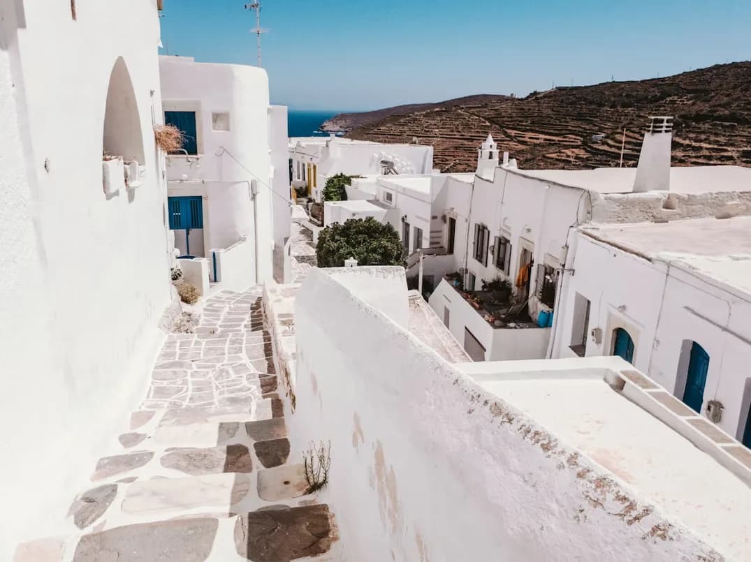 A narrow, white-washed alleyway with cobblestone stairs winds between traditional Cycladic buildings.