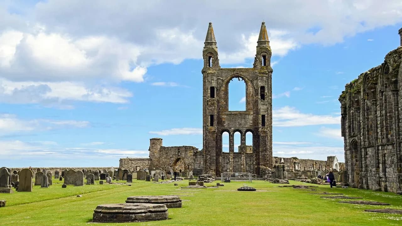 The ancient ruins of St Andrews Cathedral, with its large stone arches and bell tower, are surrounded by a grassy field and historic gravestones.
