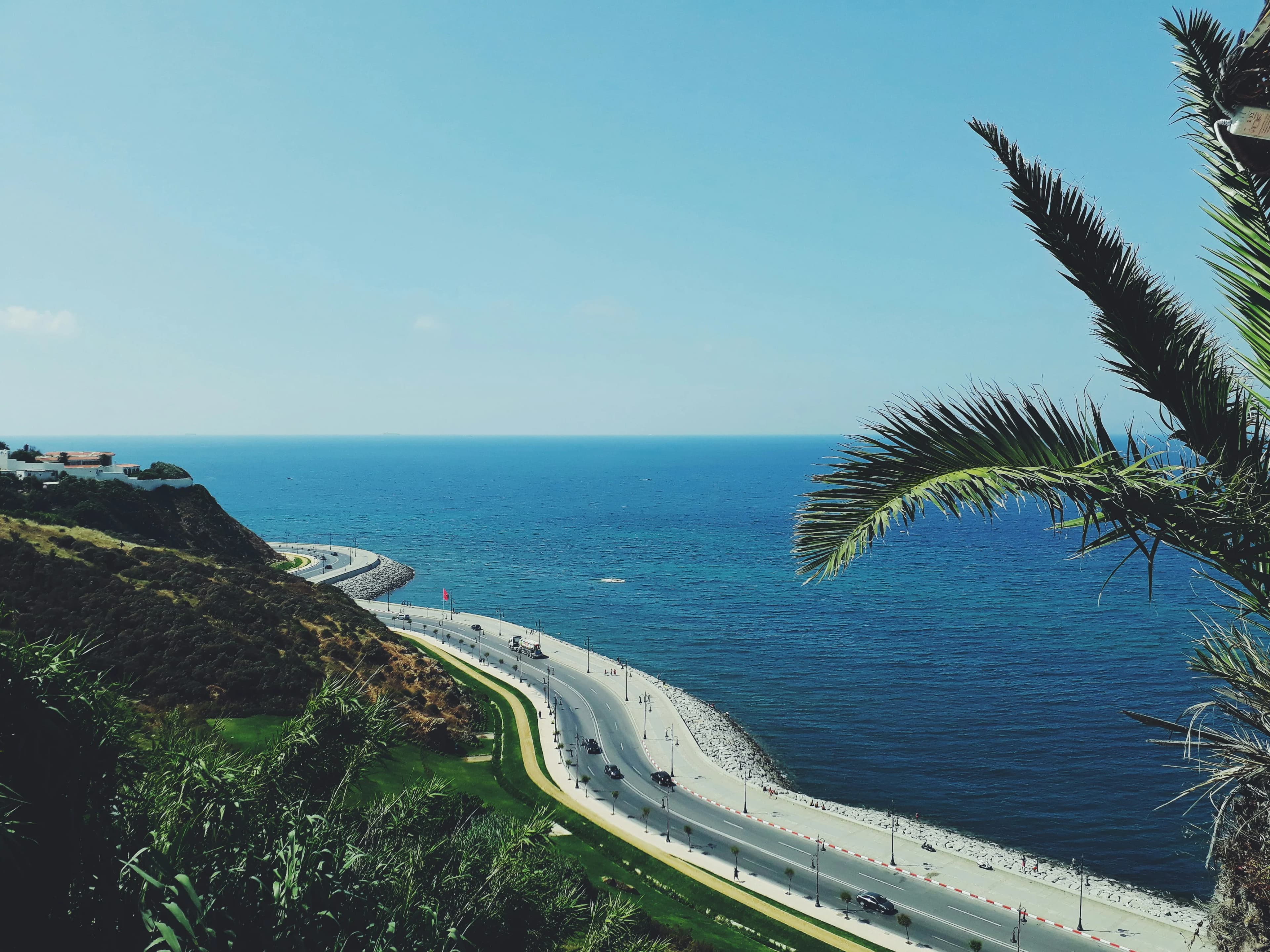 A scenic view of a coastal road winding along the cliffs of Tangier, with the vast blue ocean on one side.