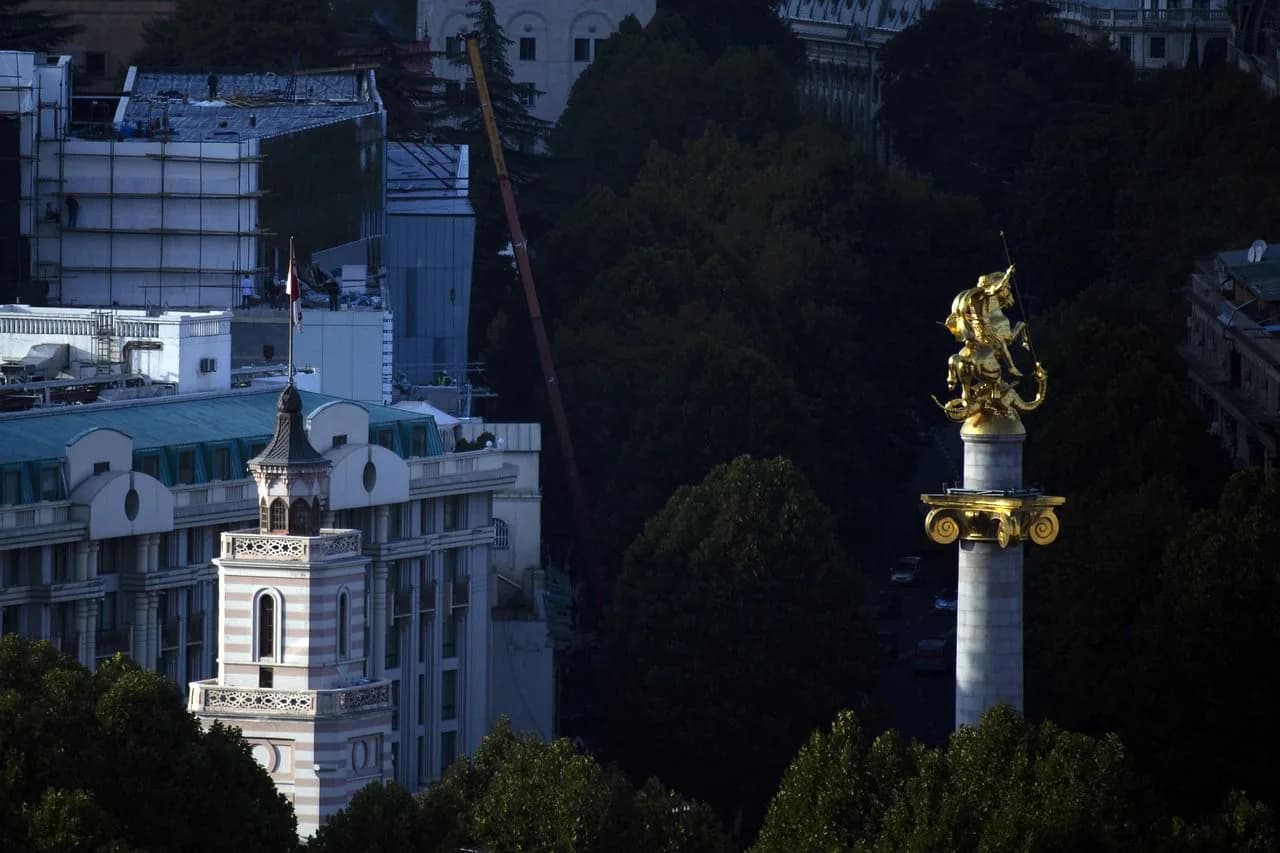 The historic Georgian Orthodox Church stands on a hill, overlooking the city's red rooftops and a wide river.