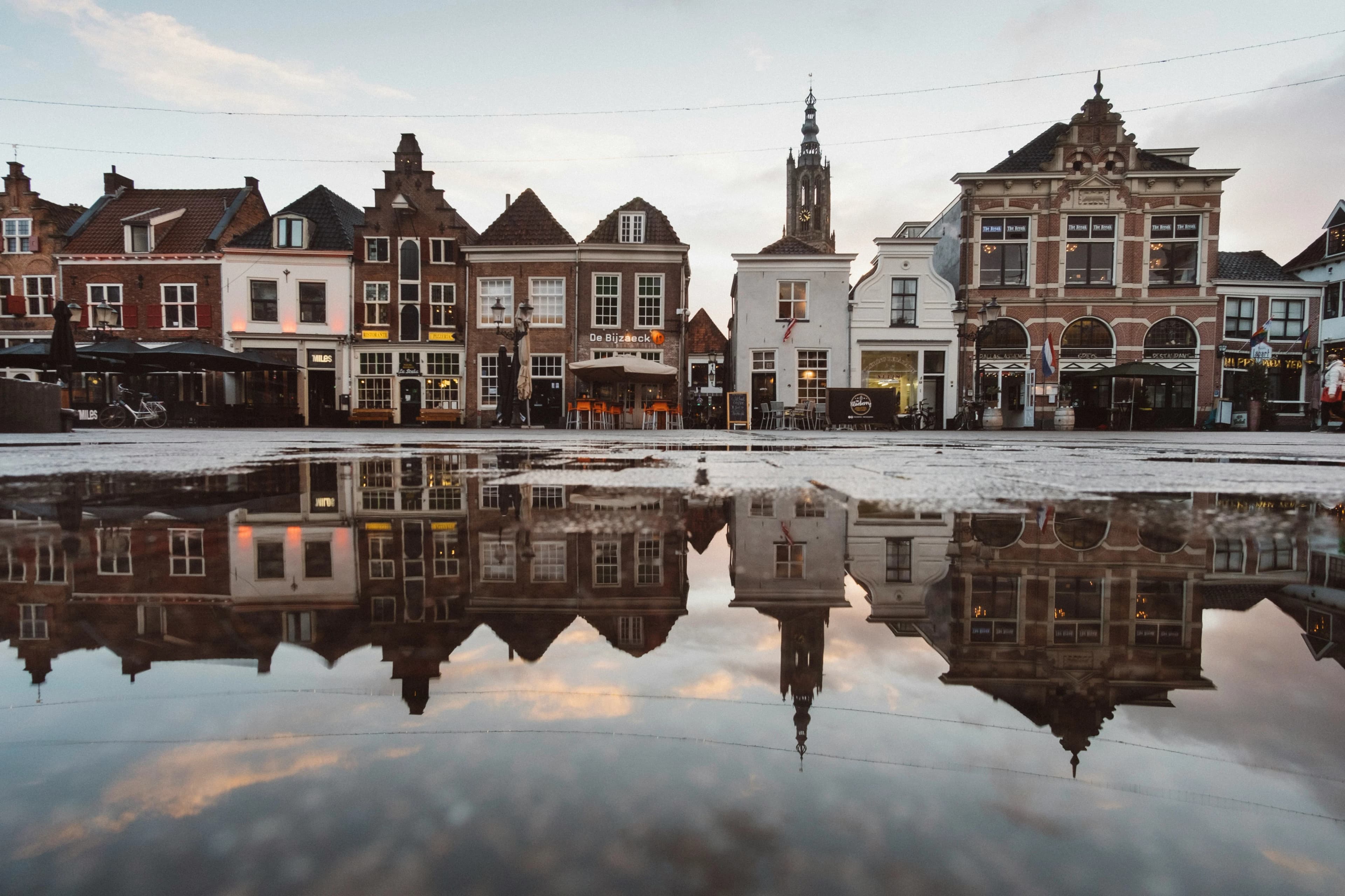 Historic buildings reflected in a puddle on a cobblestone street in Utrecht.
