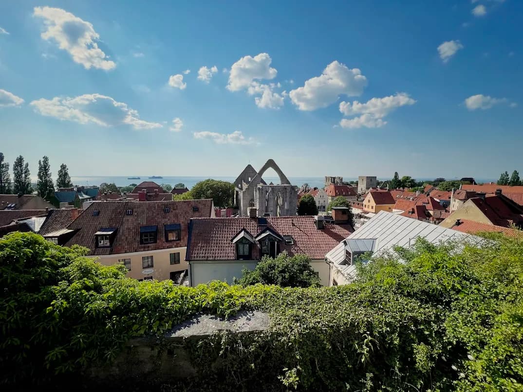 The ruins of a medieval church stand against a bright blue sky, overlooking the unique red rooftops of Visby.