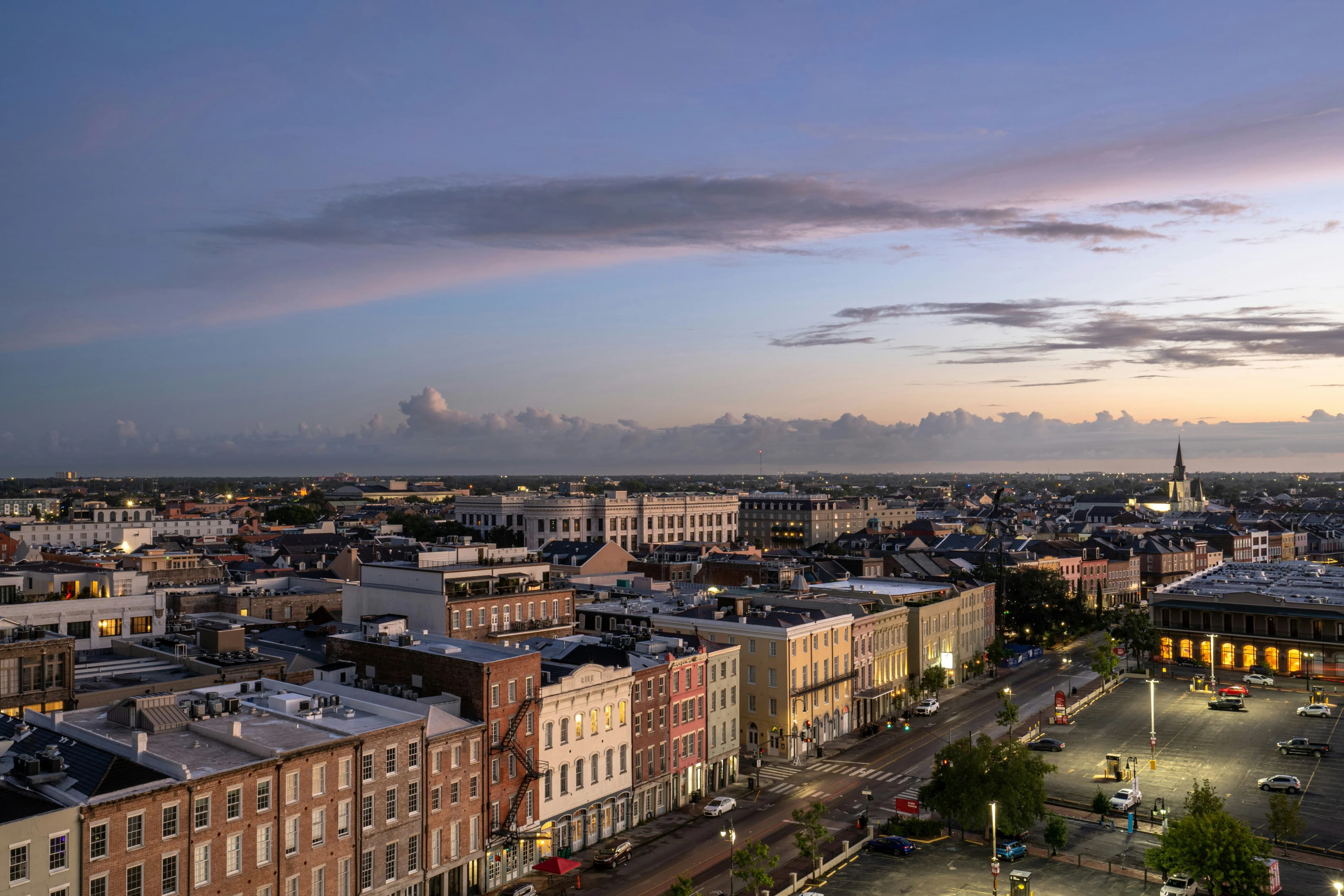 An aerial view of a lively city street at dusk, with lights beginning to glow from buildings and cars below.