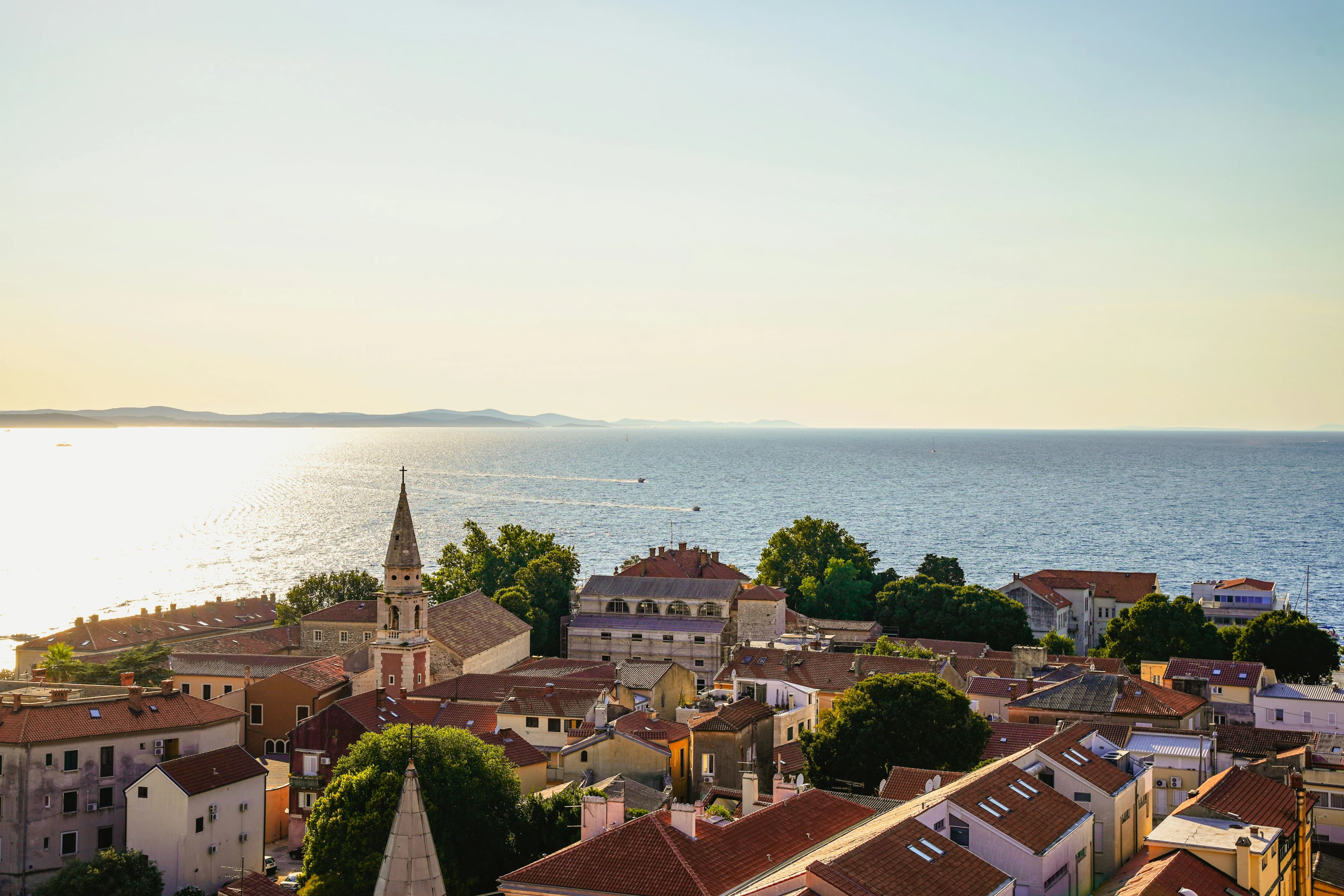 Rooftops of historic buildings lead down to the tranquil waters of the Adriatic Sea, with small boats dotting the horizon.