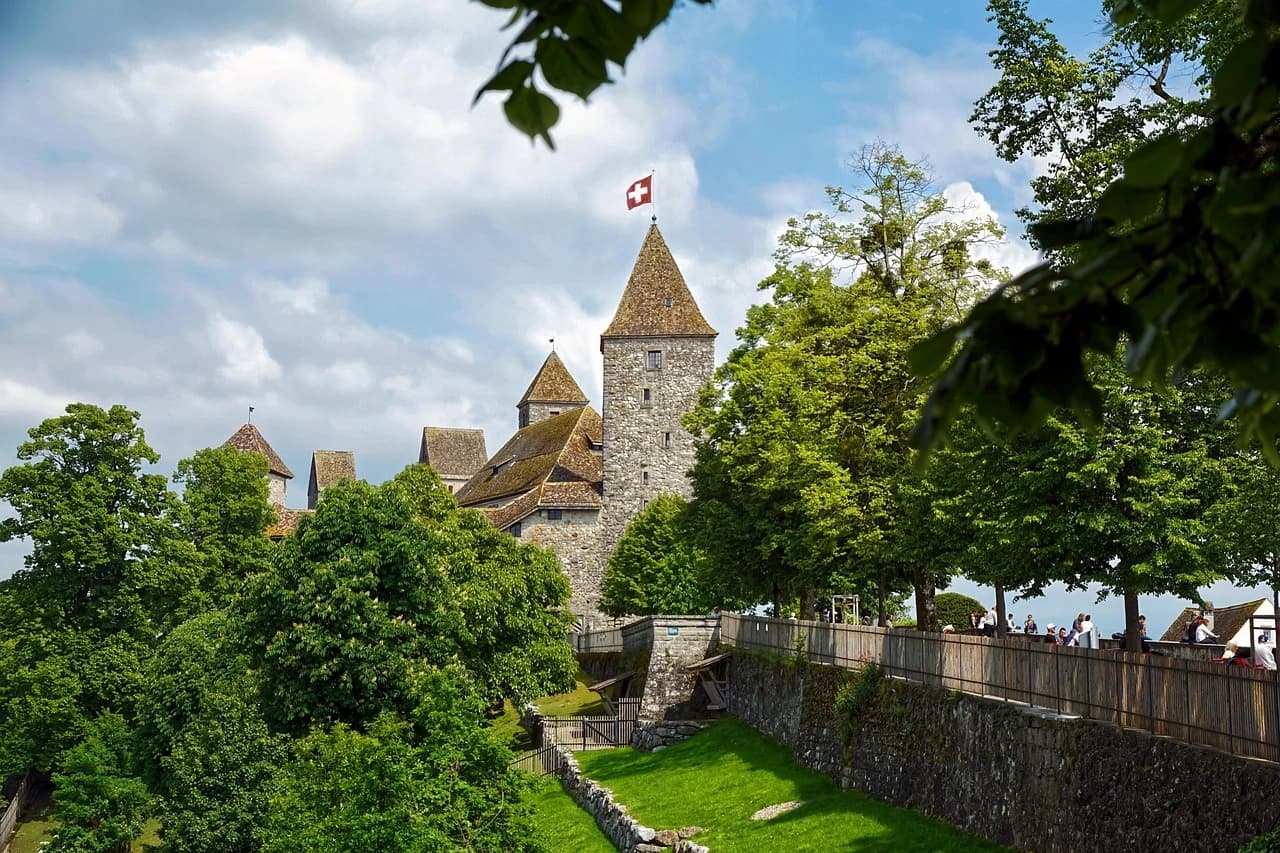The ancient Laufen Castle (Schloss Laufen) near the Rhine Falls, featuring a Swiss flag on its tower.